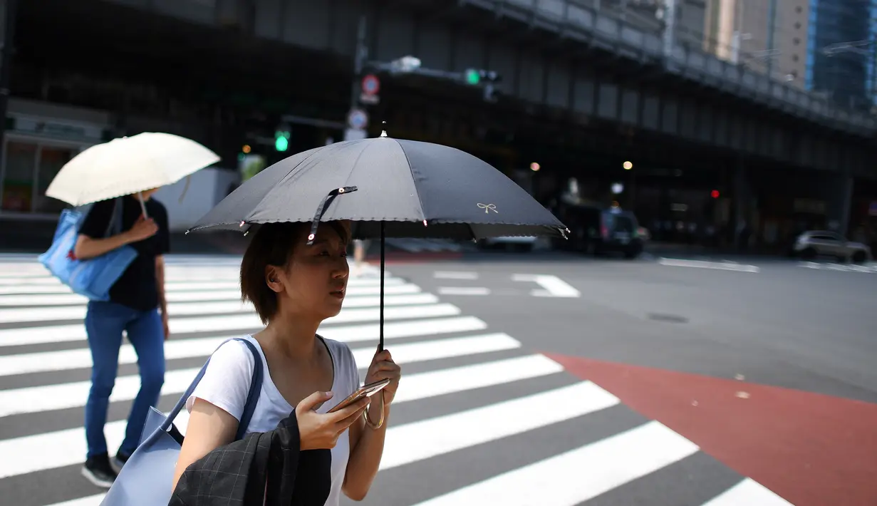 Seorang wanita melindungi dirinya dari matahari dengan payung selama gelombang panas di Tokyo, Jepang (1/8/2019). Selain Tokyo, Kota Tajimi di Perfektur Gifu, Kota Kyoto, dan Kota Hatoyama di Perfektur Saitama juga menjadi wilayah terpanas di Jepang. (AFP Photo/Charly Triballeau)