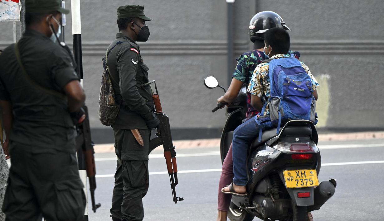 Para komuter mengendarai skuter melewati tentara yang berjaga di sepanjang jalan di Kolombo pada Sabtu (2/4/2022). Pasukan yang dipersenjatai dengan senapan serbu otomatis dikerahkan di Sri Lanka untuk mengendalikan massa, beberapa jam setelah presiden menyatakan keadaan darurat. (KODIKARA / AFP)