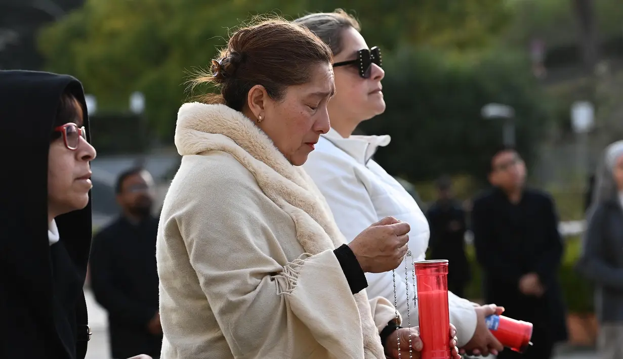 Orang-orang berdoa di depan patung Yohanes Paulus II di luar rumah sakit Gemelli di mana Paus Fransiskus dirawat karena pneumonia di Roma, pada 23 Februari 2025. (Isabella BONOTTO/AFP)