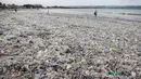 Volume sampah kiriman mencapai puluhan ton per hari, yang didominasi oleh limbah plastik dan potongan kayu. Tampak dalam foto, para pekerja dan warga membersihkan ceceran dan tumpukan sampah plastik yang terdampar di Pantai Jimbaran, Bali, pada Selasa 10 Maret 2026. (Lana Priatna/AFP)