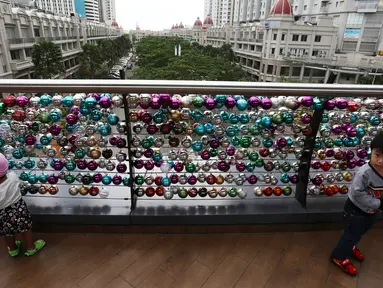 Anak-anak bermain di depan ribuan Bola bertuliskan harapan yang tergantung di pagar jembatan Eco Skywalk di Mall Central Park, Jakarta, Senin (19/12). Pengunjung dapat membeli Bola Pengharapan dengan harga Rp. 10.000. (Liputan6.com/Johan Tallo)