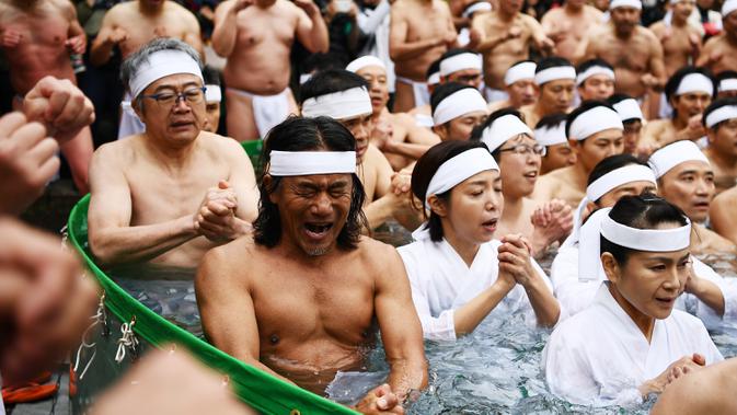 RITUAL MENYUCIKAN DIRI - Orang-orang percaya Shinto dari Kuil Teppozu Inari mandi dengan air dingin untuk menyucikan jiwa dan tubuh mereka selama ritual Tahun Baru di Tokyo, Minggu (12/1/2020). Sekitar 100 orang percaya Shinto ambil bagian dalam ritual tahunan tersebut. (AFP/Charly Triballeau)