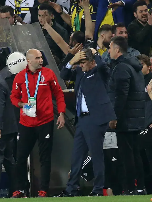 Pelatih Besiktas Senol Gunes memegangi kepalanya setelah terkena lemparan benda tajam dari tribun penonton pada semifinal Piala Turki melawan Fenerbahce di Istanbul, Kamis (19/4). Pertandingan memanas usai pemain Besiktas, Pepe diganjar kartu merah. (AFP)
