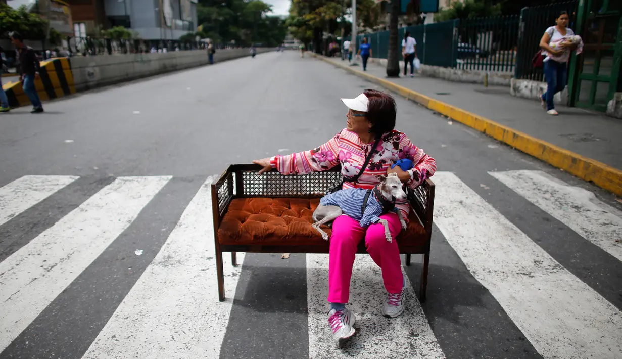 Seorang wanita duduk dengan anjingnya di sebuah sofa yang berada di tengah jalan saat unjuk rasa memprotes anti-pemerintah Nicolas Maduro di Caracas, Venezuela, (20/7). (AP Photo / Ariana Cubillos)