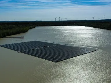 Pemandangan dari udara menunjukkan panel surya dengan turbin angin di kejauhan di pabrik fotovoltaik terapung di danau Silbersee di Haltern, Jerman barat (22/4/2022). Taman surya terapung terbesar di Jerman saat ini sedang dibangun. (AFP/Ina Fassbender)