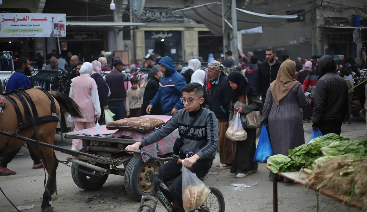 Tahun 2026 menjadi yang ketiga masyarakat Gaza merayakan Idul Fitri di tengah situasi konflik yang berkepanjangan sejak Oktober 2023. Tampak dalam foto, seorang anak laki-laki Palestina yang mengungsi mengendarai sepeda sementara orang-orang berbelanja di kios-kios di pasar jalanan sekitar kamp pengungsi Nuseirat, Jalur Gaza tengah, pada Rabu 18 Maret 2026. (Eyad Baba/AFP)