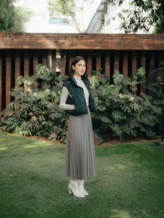 Yasmin Napper nampak anggun dengan padu padan turtleneck long sleeve top warna beige, dipadukan quilted vest hitam, rok plisket abu-abu, dan sepatu boots warna beige.  [@yasminnapper].