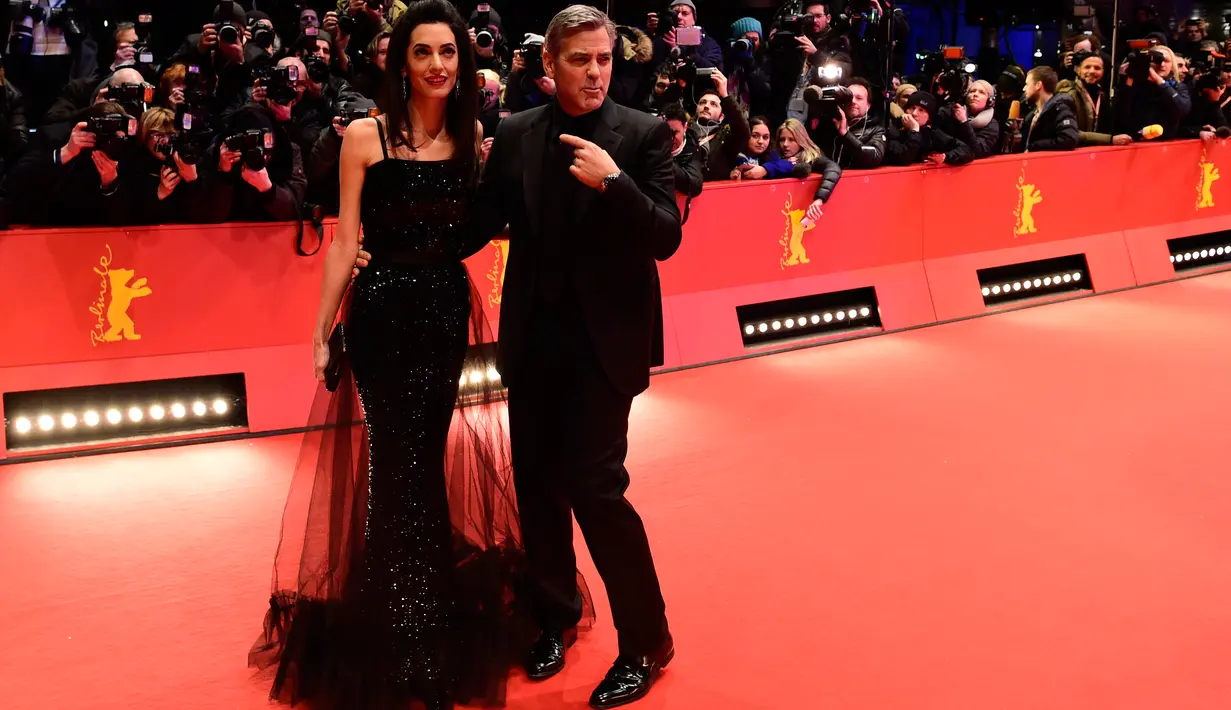 George Clooney merangkul pinggang istrinya, Amal Alamuddin, saat berpose untuk fotografer di karpet merah pemutaran film "Hail, Caesar!" pada pembukaan Berlin International Film Festival ke-66 di Berlin, Jerman, Kamis (11/2). (John MACDOUGALL/AFP)