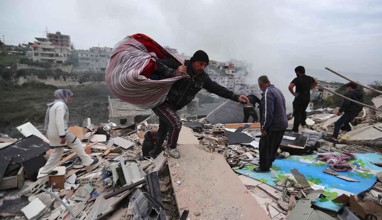 Warga mengumpulkan sisa-sisa barang milik mereka dari sebuah bangunan yang hancur akibat serangan Israel di desa Qennarit, Lebanon selatan, Kamis 22 Januari 2026. Israel kembali menyerang sejumlah desa di Lebanon selatan, termasuk Qanarit, Zrariyeh, dan Ansar. (AP Photo/Mohammed Zaatari)