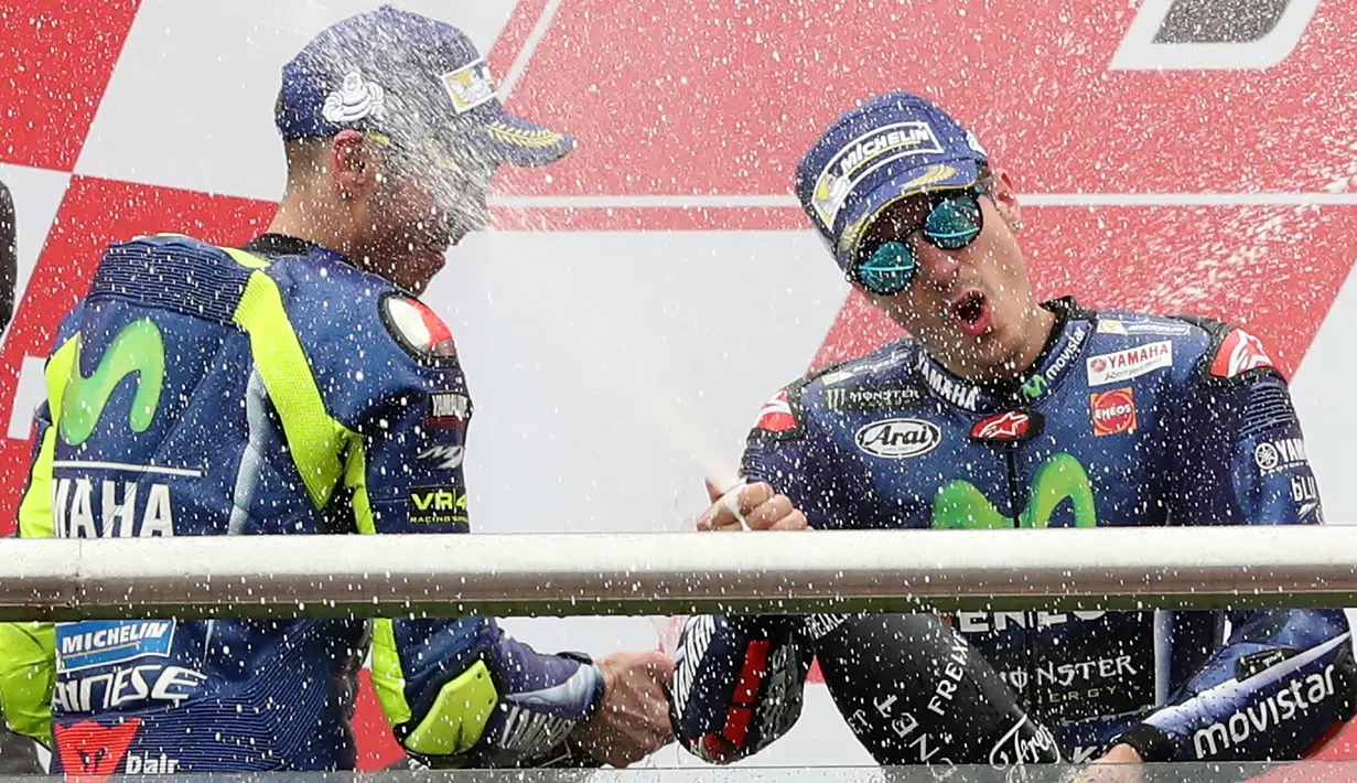 Pembalap Movistar Yamaha, Maverick Vinales merayakan kemenangannya setelah finis pertama pada MotoGP Argentina dengan menyemprotkan sampanye bersama Valentino Rossi di atas podium Sirkuit Termas de Rio Hondo, Minggu (9/4). (AP Photo/Nicolas Aguilera)