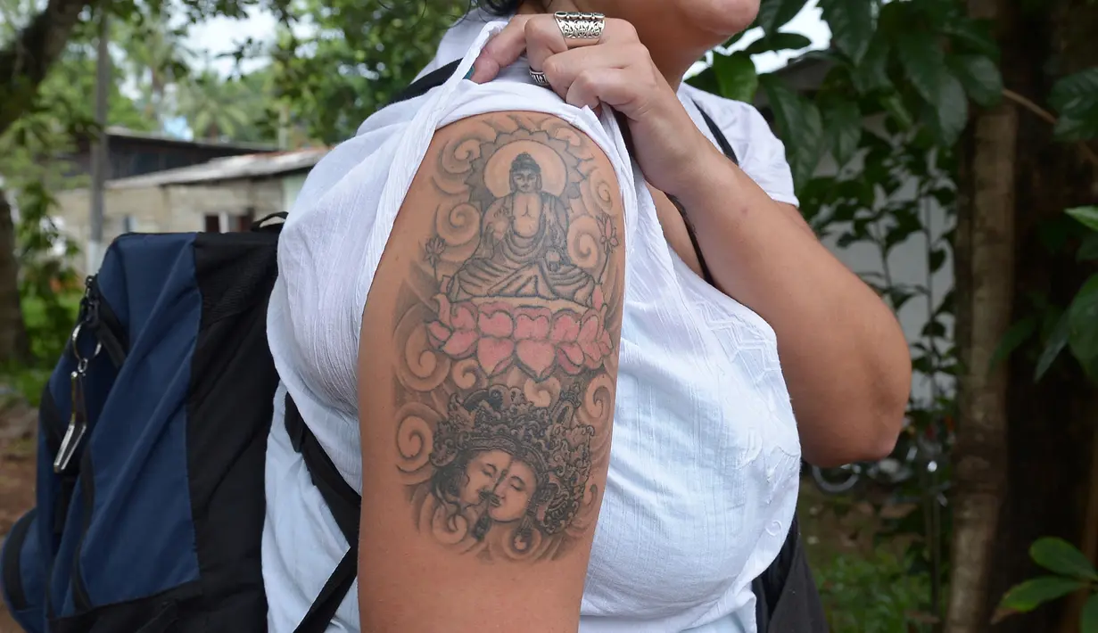 File foto pada 22 April 2014, Naomi Coleman asal Inggris memperlihatkan tato Sang Buddha di lengannya usai dideportasi dari Sri Lanka. Coleman yang sempat ditahan selama empat hari itu akhirnya mendapat uang ganti rugi. (Lakruwan WANNIARACHCHI/AFP)
