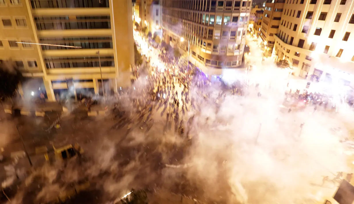 Pengunjuk rasa berlarian saat polisi menembakkan gas air mata untuk membubarkan massa selama protes menentang rencana pengenaan pajak baru di Beirut, Lebanon, Jumat (18/10/2019). Saat ini Lebanon menjadi salah satu negara dengan utang terbesar di dunia. (AP Photo/Hassan Ammar)