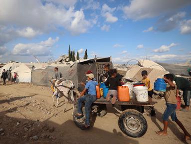 Warga dan anak-anak Palestina mengangkut jeriken berisi air bersih dari tangki air bergerak dengan gerobak keledai di kamp pengungsi Bureij di Jalur Gaza tengah pada 6 Oktober 2025. (Eyad BABA/AFP)