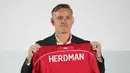 Sebagai informasi, John Herdman datang ke Indonesia dengan membawa sejumlah pengalaman sukses, terutama saat bertugas di Kanada. Dia mengantar timnas putri Kanada meraih dua medali perunggu berturut-turut dalam Olimpiade 2012 dan 2016. Tampak dalam foto, pelatih kepala tim nasional sepak bola Indonesia yang baru, John Herdman memegang jersey tim yang bertuliskan namanya saat konferensi pers di Jakarta, Selasa 13 Januari 2026. (AP Photo/Achmad Ibrahim)