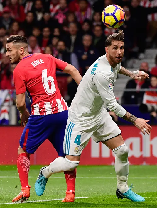 Bek Real Madrid, Sergio Ramos berebut bola dengan gelandang Atletico Madrid, Koke pada laga pekan ke-12 La Liga di Stadion Wanda Metropolitano, Sabtu (18/11). Laga Derbi Madrid itu berakhir imbang tanpa gol (CURTO DE LA TORRE/AFP)
