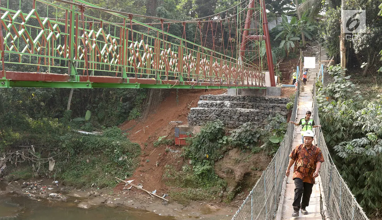 Pekerja berjalan di samping jembatan gantung yang diberi julukan Indiana Jones di Srengseng Sawah, Jagakarsa, Jakarta, Jumat (3/8). Pemprov DKI membangun jembatan Indiana Jones karena yang lama sudah tidak layak. (Liputan6.com/Immanuel Antonius)