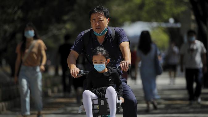 Seorang pria dan seorang anak mengenakan masker untuk membantu mengekang penyebaran virus corona COVID-19 bersepeda di Beijing, China, Senin (24/8/2020). China telah delapan hari tanpa laporan kasus baru virus corona COVID-19. (AP Photo/Andy Wong)