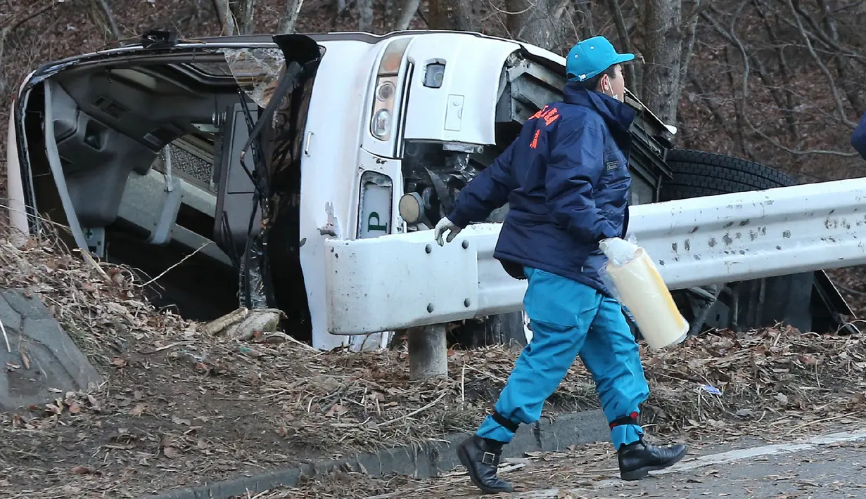 Seorang penyidik berjalan di dekat bangkai bus yang tergelincir di Karuizawa, prefektur Nagano, Jepang, Jumat (15/1). Bus yang membawa pengunjung resor ski itu tergelincir dan menewaskan 14 orang serta melukai 27 lainnya. (AFP PHOTO/Jiji Press JAPAN OUT)
