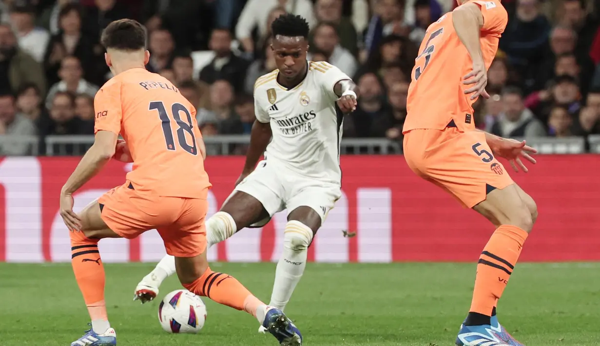 Pemain Real Madrid, Vinicius Junior berusaha melewati pemain Valencia pada laga Liga Spanyol di Stadion Santiago Bernabeu, Sabtu (11/11/2023). Berkat kemenangan ini, Real Madrid tetap berada di peringkat dua klasemen sementara La Liga, sementara Valencia tertahan di peringkat 10. (AFP/Thomas Coex)