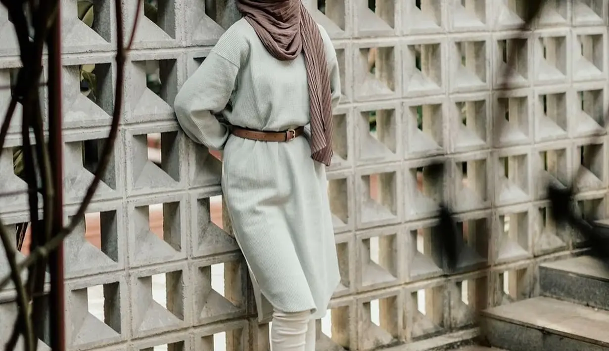 Tunik berbahan rajut makin kece ditambahkan leather belt dan white mules yang manis.  [Instagram/adiba.knza]