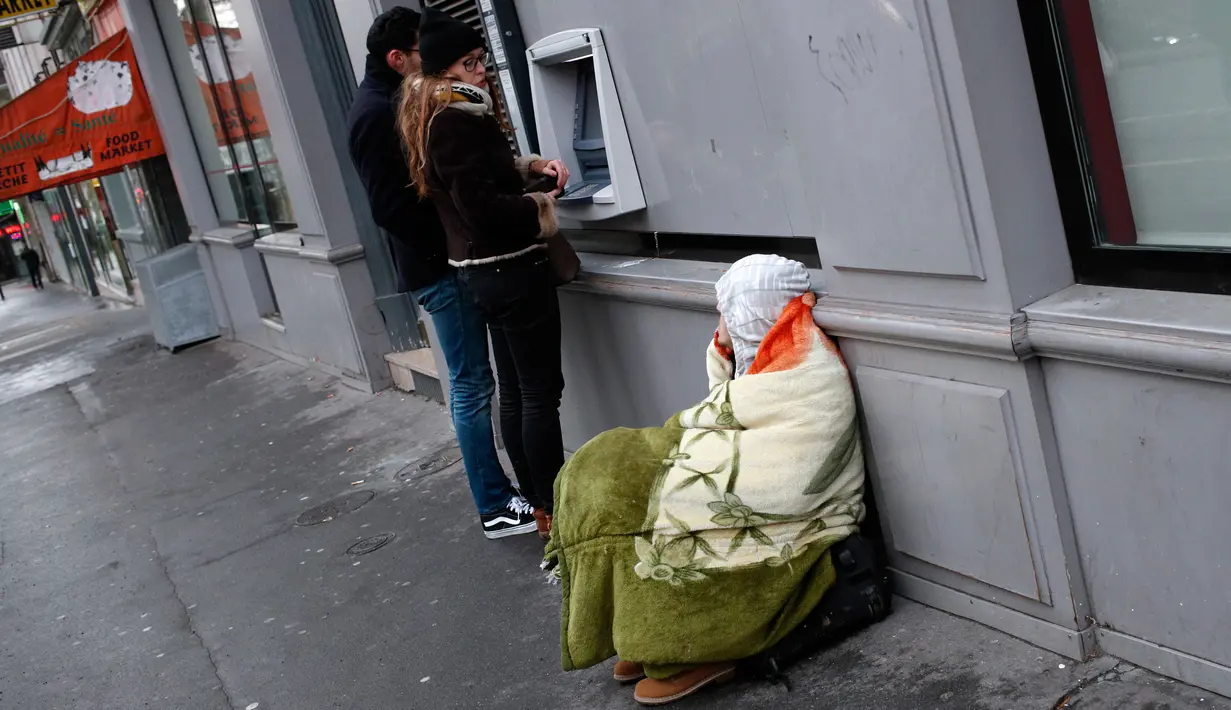 Seorang tunawisma duduk di samping mesin ATM di Paris, Prancis, Senin (5/2). (AP Photo / Francois Mori)