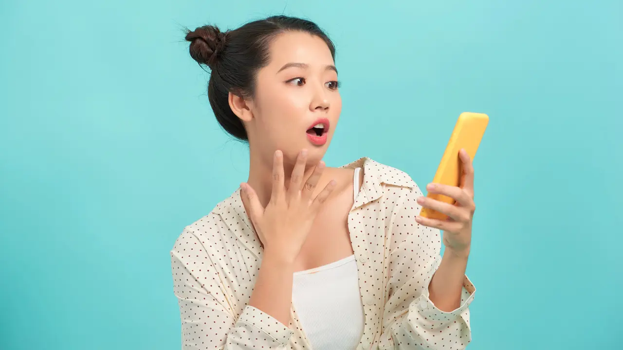 Wanita muda asia memegang handphone dengan wajah terkeju