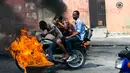 Pengendara sepeda motor melewati barikade ban yang terbakar saat terjadi protes krisis bahan bakar di Port-au-Prince, Haiti, Senin (16/9/2019). Krisis bahan bakar menyebabkan transportasi umum tidak beroperasi. (AP Photo/Dieu Nalio Chery)