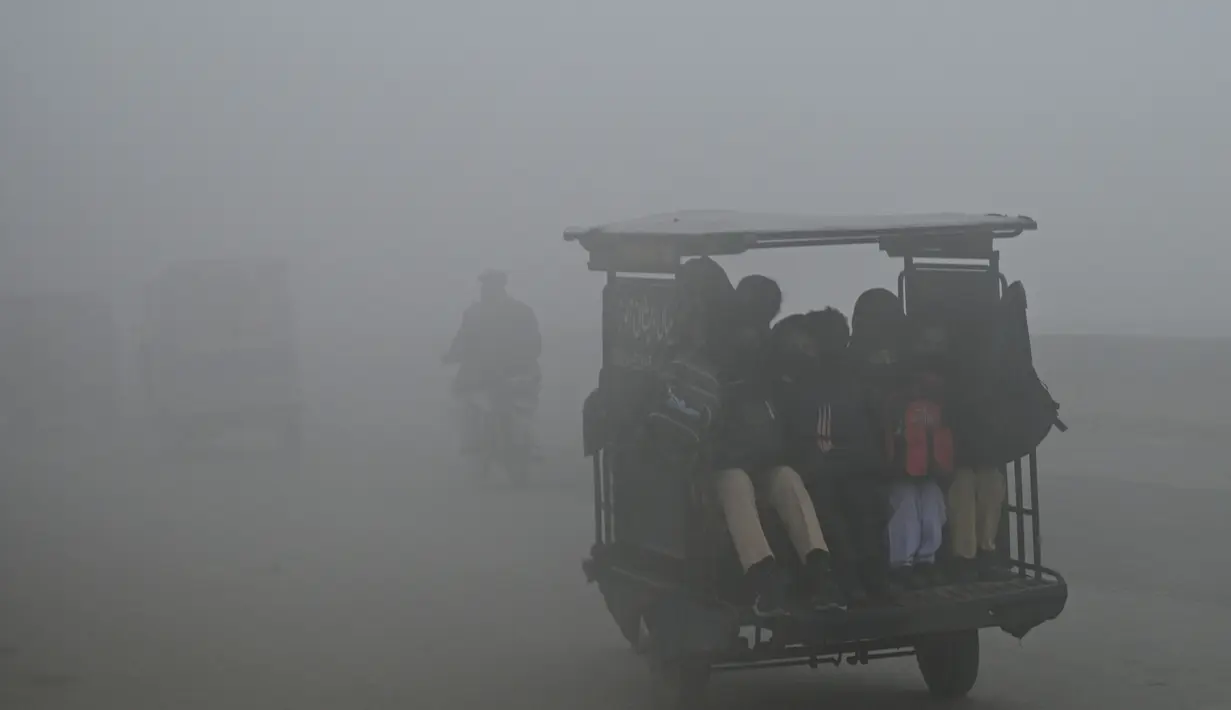 Siswa duduk di atas becak saat dalam perjalanan ke sekolah di tengah cuaca berkabut di Lahore (21/12/2022). Beberapa penerbangan dialihkan ke bandara lain akibat cuaca berkabut. (AFP/Arif Ali)