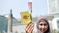 Seorang wanita menunjukkan bunga mawar dan buku panduan saat peringatan Hari AIDS Sedunia di Bundaran HI, Jakarta, Minggu (1/12/2019). Kegiatan ini bertujuan mengedukasi masyarakat tentang penyakit AIDS dan mengajak untuk peduli serta tidak menjauhkan penderita AIDS. (merdeka.com/Iqbal S. Nugroho)