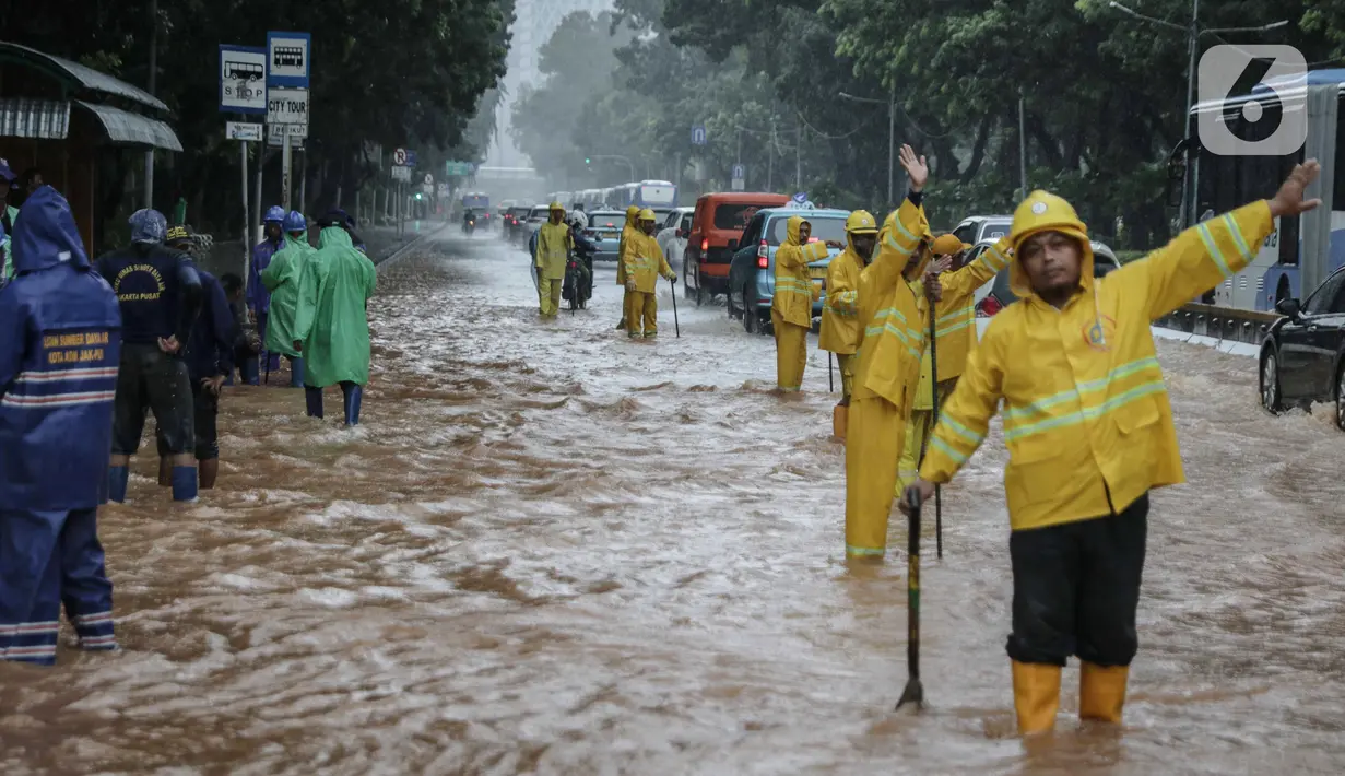 Petugas mengatur lalu lintas saat air menggenangi Jalan Medan Merdeka Barat, Jakarta, Kamis (24/1/2020). Hujan deras yang mengguyur Jakarta sejak pagi tadi mengakibatkan genangan air di Jalan Medan Merdeka Barat. (Liputan6.com/Faizal Fanani)