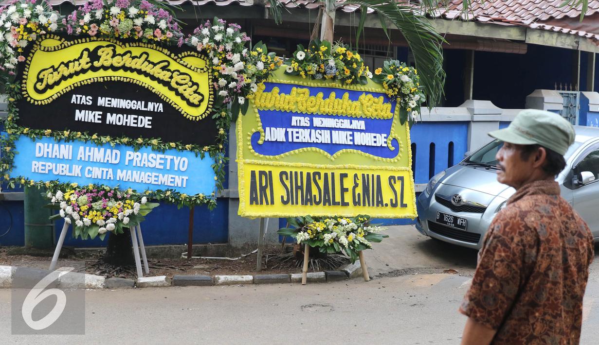 Warga melintasi karangan bunga duka cita wafatnya penyanyi Mike Mohede di kawasan Tangerang Selatan, Banten, Senin (1/8). Mike Mohede mengembuskan napas terakhirnya saat tidur siang di kamar seusai bermain game. (Liputan6.com/Herman Zakharia)