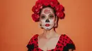 Wajahnya dirias dengan makeup tengkorak tradisional yang dikenal sebagai “calavera,” lengkap dengan detail rumit dan bunga mawar pada dahinya, mencerminkan penghormatan kepada roh leluhur dalam perayaan ini. [@itsmebcl].