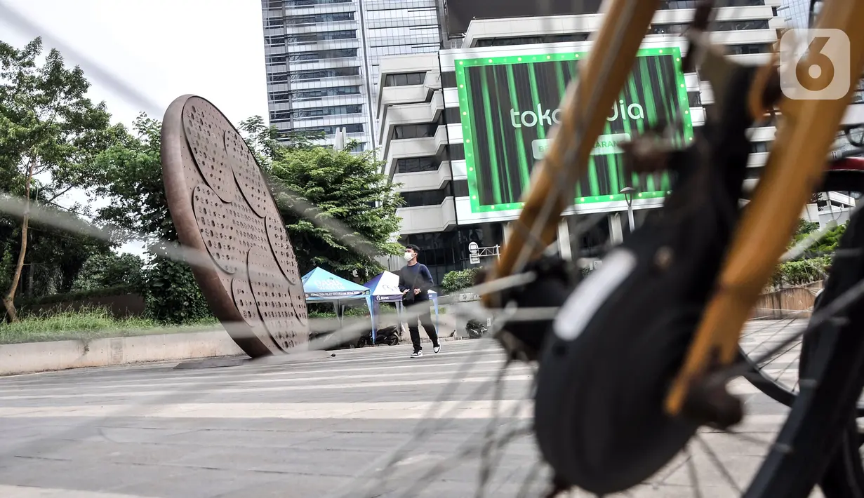Pejalan kaki melintas dekat Tugu Sepeda di Jalan Jenderal Sudirman, Jakarta Pusat, Minggu (23/10/2022). Biaya pembangunan Tugu Sepeda masuk ke dalam anggaran pembuatan jalur sepeda permanen di Jalan Sudirman - Thamrin oleh pihak swasta sebesar Rp 28 miliar. (merdeka.com/Iqbal S. Nugroho)
