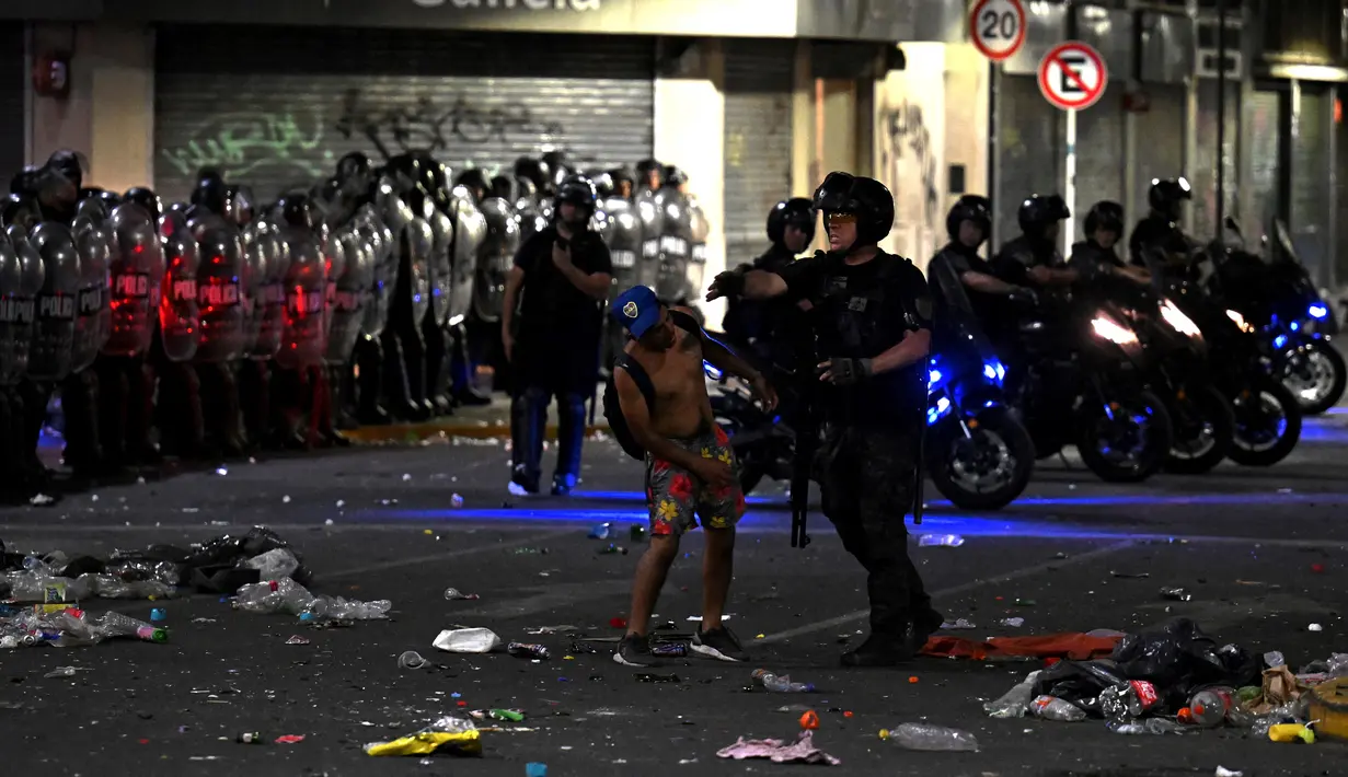 Seorang polisi anti huru hara menghadapi seorang suporter Argentina selama bentrokan setelah perayaan timnas Argentina meraih juara Piala Dunia Qatar 2022 di lingkungan Obelisk di Buenos Aires (20/12/2022). (AFP/Luis Robayo)