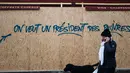 Seorang wanita berjalan melewati grafiti bertuliskan 'kami ingin seorang presiden untuk orang miskin' di sebuah toko dekat Arc de Triomphe, Paris, Prancis,  Minggu (2/12). Tiga orang tewas dalam unjuk rasa sejak dua pekan lalu. (AP Photo/Kamil Zihnioglu)