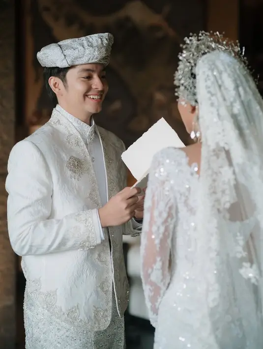Angga terlihat tampan dalam balutan setelan pengantin putih. Shenina juga tampak anggun dengan gaun pernikahan elegan. Senyum Angga menunjukkan kebahagiaan yang terpancar jelas di hari pernikahan, menandai dirinya sudah resmi menyandang status sebagai suami. (Liputan6.com/IG/@angga)