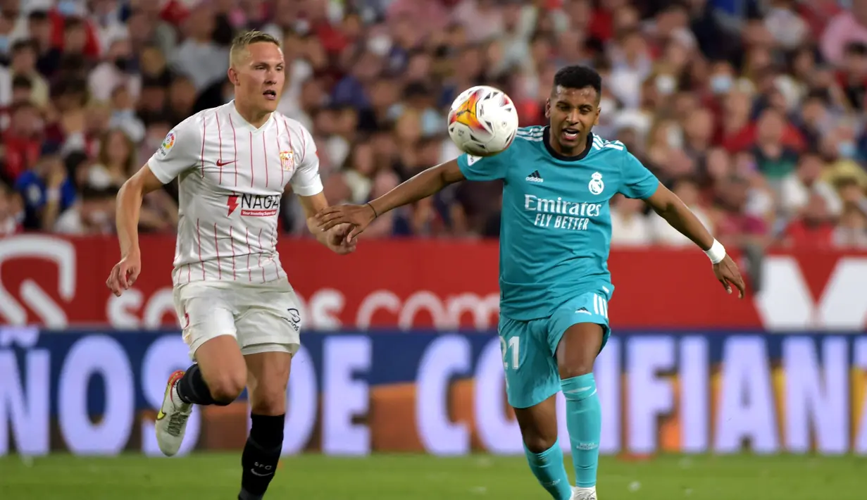Pemain depan Real Madrid Rodrygo (kanan) berebut bola dengan bek Sevilla Ludwig Augustinsson pada lanjutan Liga Spanyol di stadion Ramon Sanchez Pizjuan, Senin (18/4/2022) dini hari WIB. Real Madrid sukses menaklukkan Sevilla 3-2. (CRISTINA QUICLER / AFP)