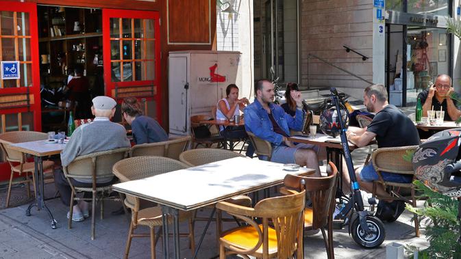 Orang-orang duduk di luar sebuah kafe di kota pantai Mediterania Israel di Tel Aviv, Rabu (27/5/2020). Setelah lebih dari dua bulan, Israel pertama kalinya mengizinkan restoran hingga kafe dibuka kembali usai pelonggaran pembatasan yang diberlakukan untuk mencegah Covid-19. (JACK GUEZ/AFP)