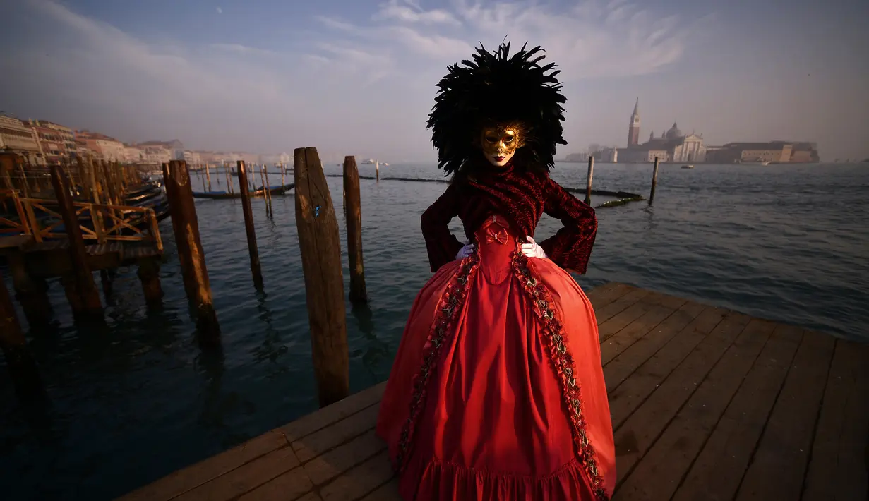 Peserta dengan dominasi kostum warna merah hitam dan topeng emas berdiri di St Mark Square selama Karnaval Venesia di Italia, Sabtu (28/1). Tema "Creatum: Civitas Ludens" dapat diterjemahkan sebagai "Kreativitas: Kota Olahraga". (FILIPPO MONTEFORTE/AFP)