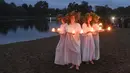 Gadis-gadis Belarusia memegang lilin saat berdiri di Sungai Berezina pada Hari Ivan Kupala di Desa Parichi, sekitar 200 km (125 mil) selatan Parichi, Belarusia, 6 Juli 2022. Hari Ivan Kupala merupakan sebuah perayaan malam kuno yang menandai Titik Balik Matahari Musim Panas, malam terpendek tahun ini. (AP Photo/Viktor Drachev)