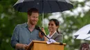 Meghan Markle memayungi Pangeran Harry saat memberi sambutan dalam kunjungan ke Victoria Park, Dubbo, Australia, Rabu (17/10). Keduanya diagendakan tur ke Australia dan Pasifik Selatan selama 16 hari. (Ian Vogler/Pool via AP)