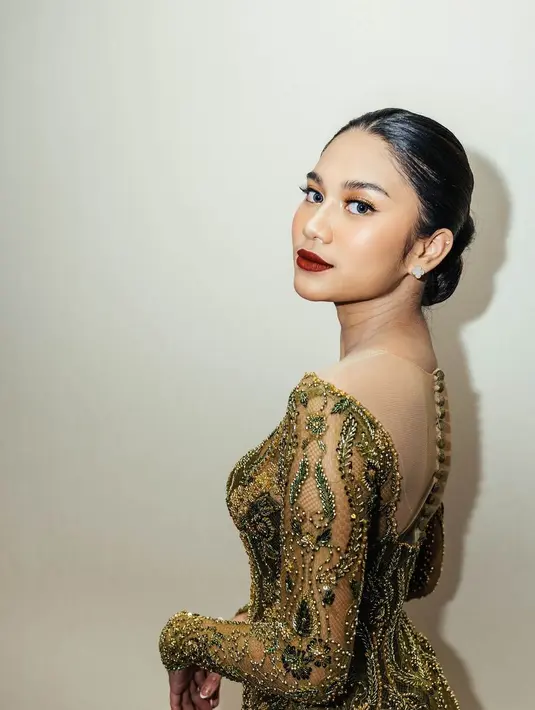 Area matanya dipertajam dengan winged eyeliner tipis, rambutnya ditata sleek look dengan sanggul rendah dan pulasan lipstik merah. [Foto: Instagram/azizahsalsha_]