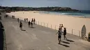 Orang-orang berjalan melewati Pantai Bondi yang kosong setelah ditutup oleh pihak berwenang di Sydney, Minggu (22/3/2020). Otoritas Australia menutup Bondi Beach  lantaran orang-orang mengabaikan larangan tidak berkumpul dalam jumlah besar untuk menekan penyebaran virus corona. (PETER PARKS/AFP)