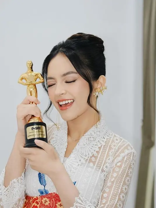 Sambil memegang piala kemenangan, Eca Aura memilih mengenakan kebaya putih dengan aksen bordiran bunga ditambah bordiran warna bunga biru di bagian bawah. Dipadukan inner putihnya.  [elsaajapasal]