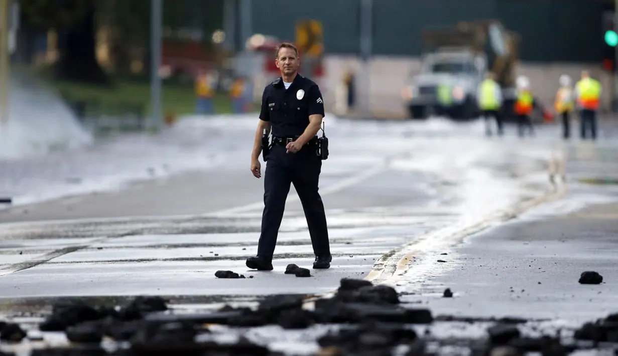 Seorang anggota kepolisian berjalan melintasi pecahan aspal akibat rusaknya pipa utama saluran air bawah tanah di sekitar Sunset Boulevard di bagian Westwood Los Angeles, (29/7/2014). (REUTERS/Danny Moloshok)
