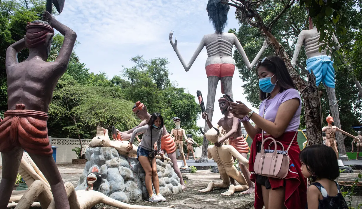 Para pengunjung mengambil foto di depan patung-patung yang menggambarkan nasib orang-orang yang tidak menjunjung tinggi lima ajaran Buddha di sebuah taman yang menggambarkan neraka versi Buddha di kuil Wat Saeng Suk di provinsi pantai Thailand Chonburi (9/7/2020). (AFP/Lillian Suwanrumpha)