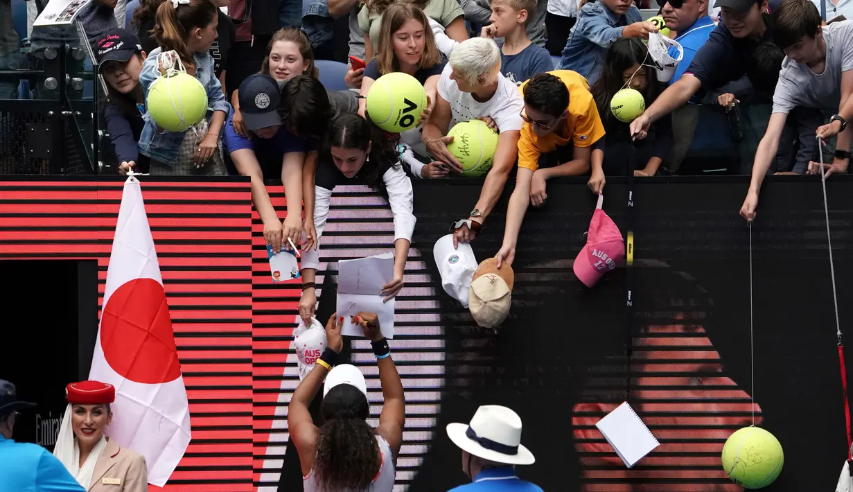 Petenis Jepang Naomi Osaka menandatangani benda yang disodorkan penonton usai mengalahkan petenis Republik Ceko Marie Bouzkova pada Australia Terbuka di Melbourne, Australia, Senin (20/1/2020). Penonton menyodorkan topi, bendera, hingga bola untuk ditandatangani Naomi. (AP Photo/Lee Jin-man)