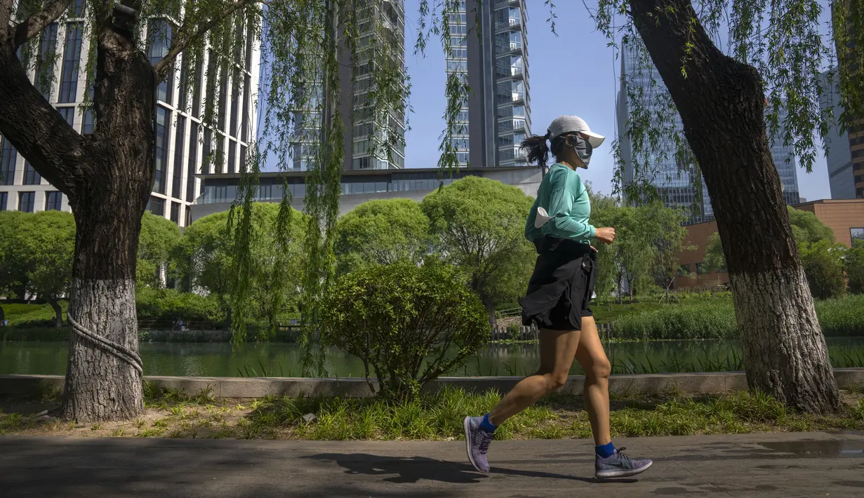 Seorang perempuan mengenakan masker berlari di sepanjang jalur air di Beijing, China, Selasa (17/5/2022). Pada Minggu (15/5) kemarin, Beijing memperpanjang aturan untuk bekerja dari rumah di empat distrik. Itu sudah melarang layanan makan di restoran dan membatasi transportasi umum, di antara langkah-langkah lainnya. (AP Photo/Mark Schiefelbein)