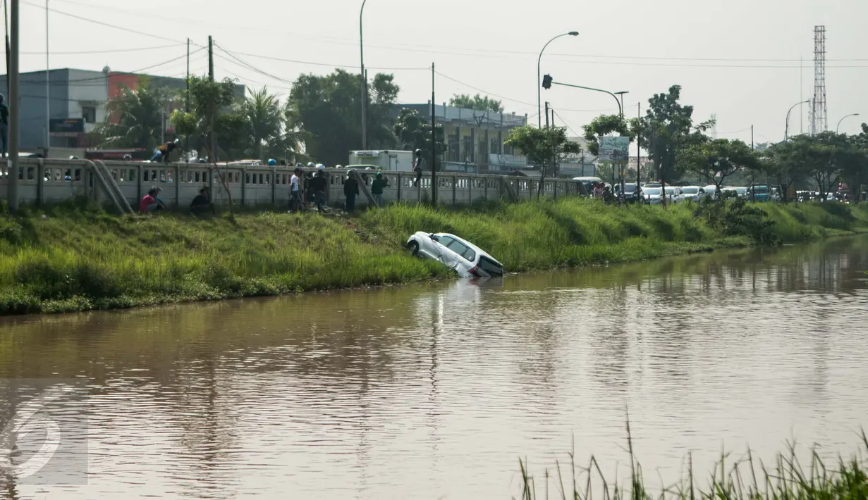 Warga menyaksikan proses evakuasi mobil yang terperosok di saluran Ispeksi Kalimalang, Jabar, Minggu (7/5). Minibus bernopol B 1475 FRK itu tercebur kedalam saluran inspeksi Kalimalang dan sempat terseret arus sejauh 100m. (Liputan6.com/Gempur M Surya)