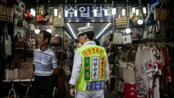 Seorang pria mengenakan rompi saat mengiklankan pakaian, sepatu, dan tas di luar sebuah toko di pasar Namdaemun di Seoul (2/7/2019). Dibangun pada tahun 1946, Pasar Namdaemun merupakan salah satu pasar tradisional yang terbesar di Korea. (AFP Photo/Minji Suh)